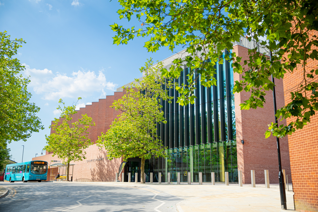 An exterior photo of Shakespeare North Playhouse, taken on a sunny day, with green trees in the foreground